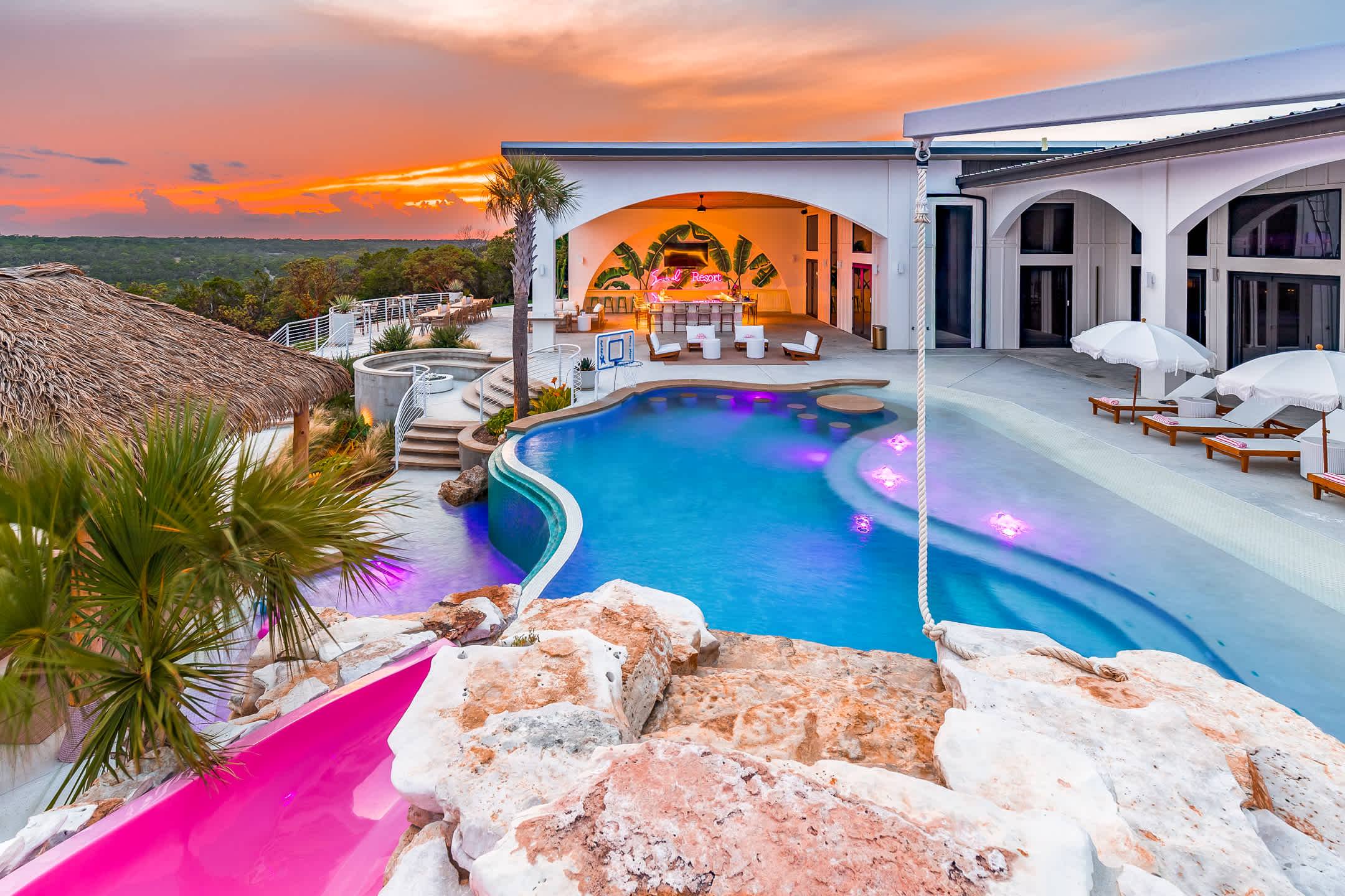 Resort-style pool, grotto, waterslide, and outdoor bar at sunset